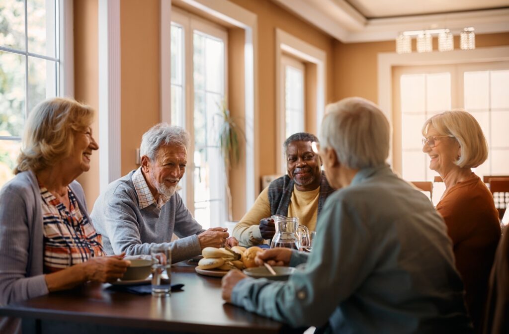 A group of older adults sitting around a table, eating and enjoying afternoon tea while smiling and chatting with each other.