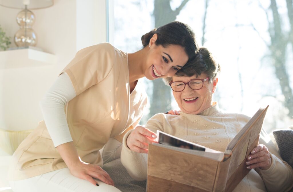 A senior woman and a caregiver smiling while looking at a photo album together.