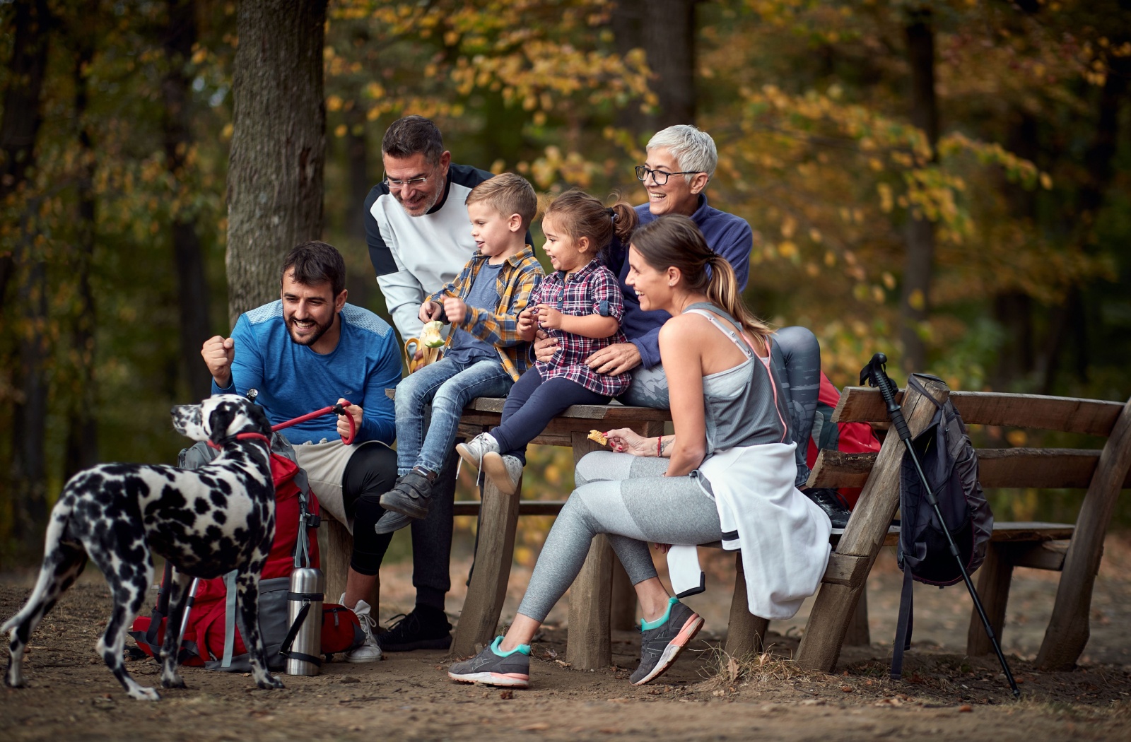 Three-generation family of two young kids, their parents, their grandparents, and a Dalmatian taking a break from their walk.