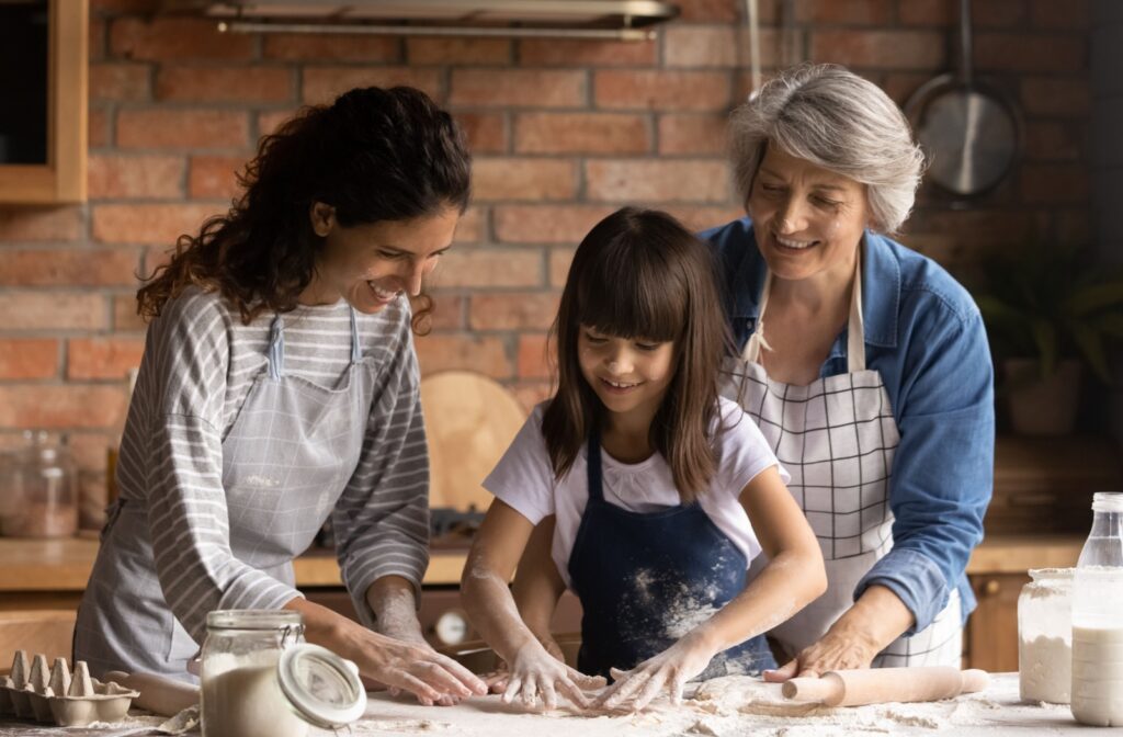 Intergenerational family of three women in a kitchen with hands covered in flour as they work together to stretch pie dough.