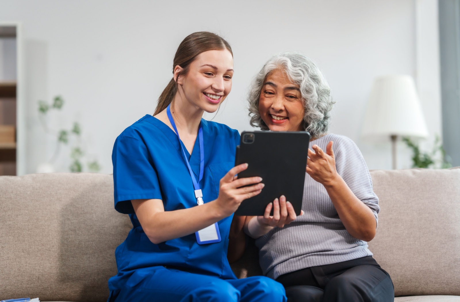 On a comfortable couch, a nurse talks to an assisted living resident through their health check with the aid of an iPad.