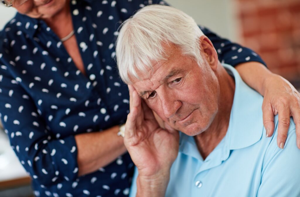 A senior with dementia touches their head while their partner consoles them.