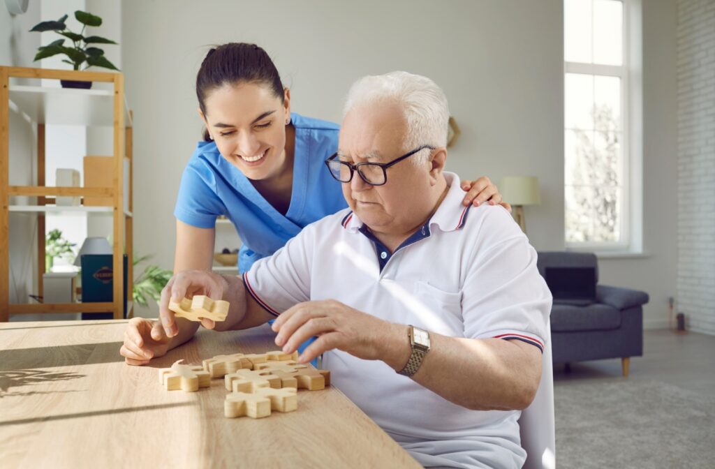 Elderly man working on a puzzle with the support of a caregiver