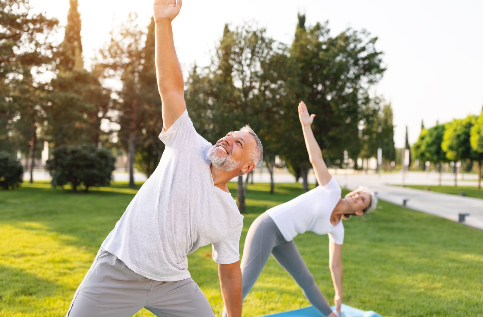 Older adults stretching outdoors on yoga mats, engaging in gentle exercise to support memory and brain health at a senior living community.