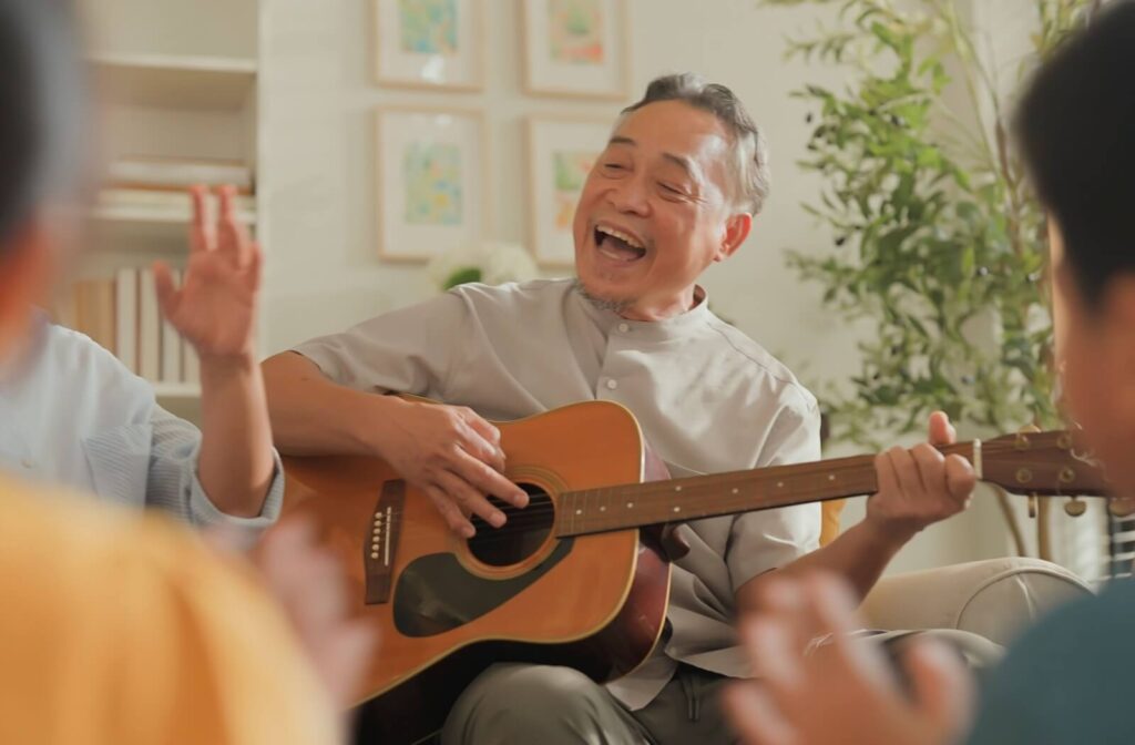 A joyful senior playing guitar and singing during a group activity at an assisted living community.