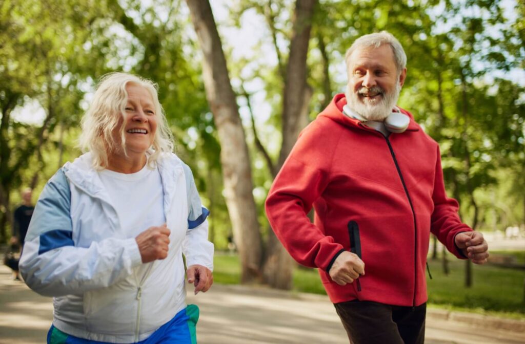 Older man in red hoodie and older woman smiling while power walking outdoors.