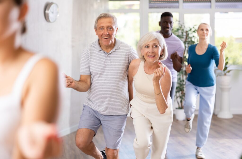 A close-up image of an older couple smiling while trying a new dance move in a group dance therapy session