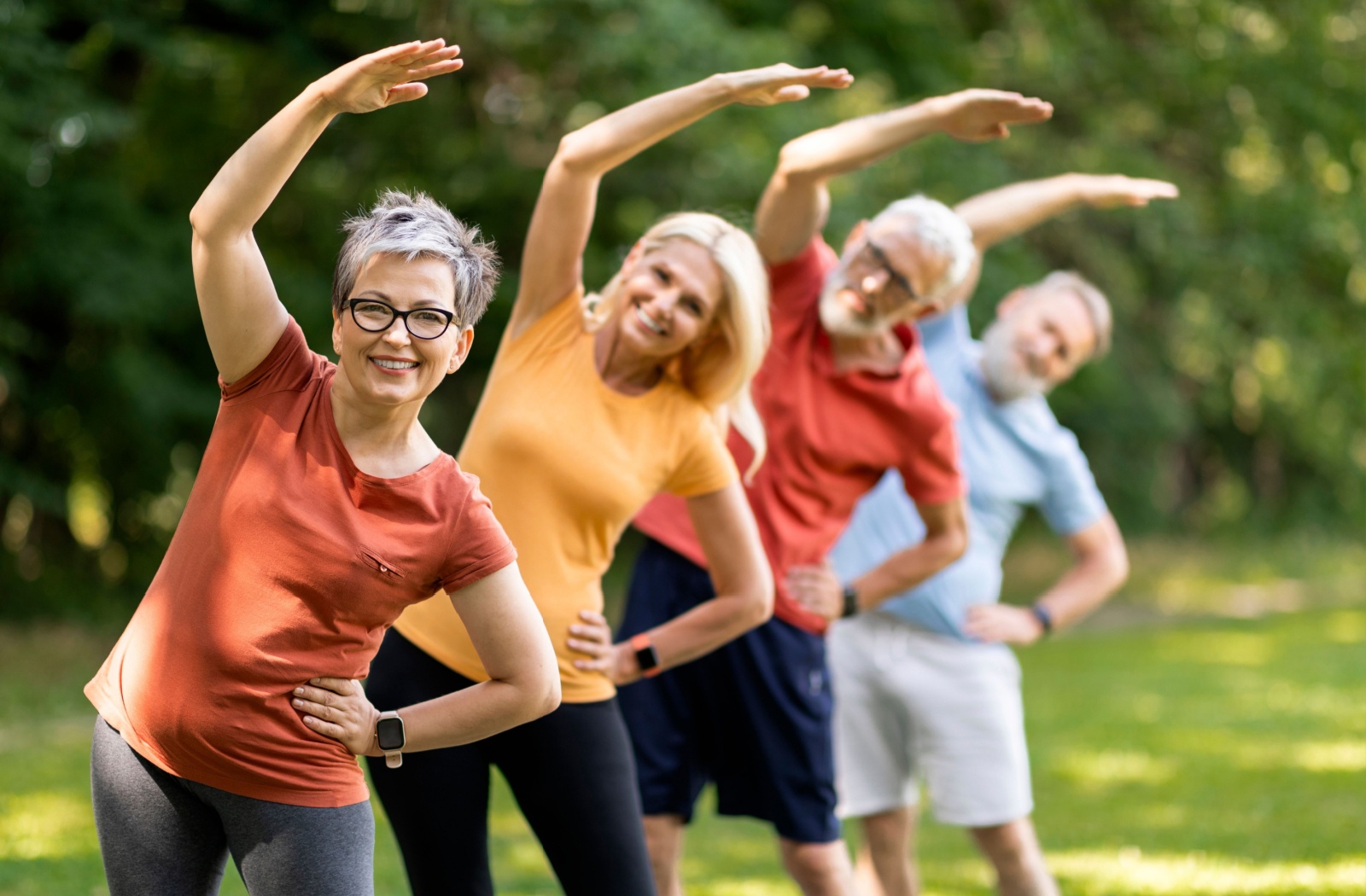 Four seniors each stretch one arm over their head as part of a warm-up stretch for walking