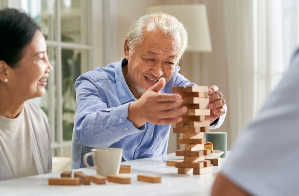 A happy senior in a blue shirt sitting at a table with a group of others playing Jenga